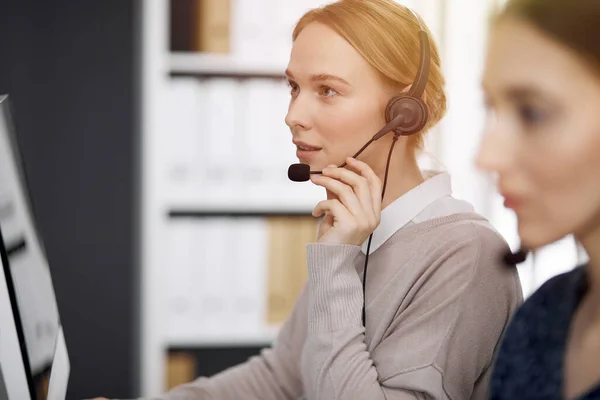 Amicale femme d'affaires caucasienne parlant par casque dans un bureau ensoleillé. Centre d'appels et divers groupes de personnes en affaires — Photo