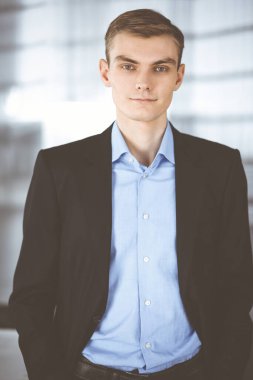 Takım elbiseli genç işadamı, modern bir ofiste dimdik dururken. İş ve iş yeri kavramı.