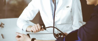 Bilinmeyen kadın doktor, klinikte birlikte otururken hastalarının kan basıncını kontrol ediyor. Coronavirus salgını sırasında ilaç konsepti. Covid 2019