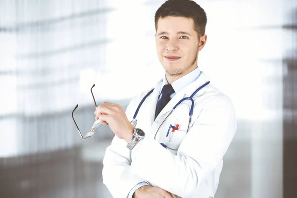 Γιατρός με γυαλιά, στέκεται με χαμόγελο στο γραφείο του νοσοκομείου. Τέλεια ιατρική υπηρεσία στην κλινική. Ευτυχές μέλλον στην ιατρική και την υγειονομική περίθαλψη — Φωτογραφία Αρχείου