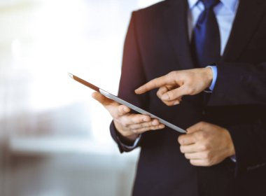 İş adamları yeni projelerini tartışmak için bir tablet bilgisayar kullanıyorlar, güneşli modern ofiste duruyorlar. İş yerinde iş arkadaşı olan tanınmamış bir işadamı ya da erkek girişimci