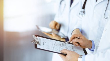 Doktorlar, iki erkek ve bir kadın, güneşli hastane ofisinde dikilen tıbbi muayene sonuçlarını tartışırlar. Doktorlar ilaç kayıtlarını doldurmak için pano kullanıyorlar. Klinikte mükemmel bir sağlık hizmeti