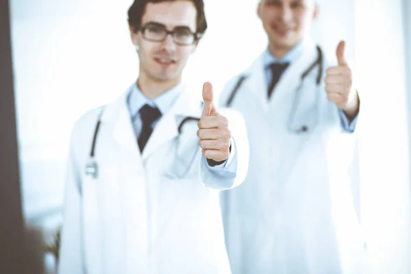 Due medici di sesso maschile in piedi come una squadra e mostrando pollici in su come simbolo del miglior servizio per i pazienti della clinica. Medicina e assistenza sanitaria — Foto Stock