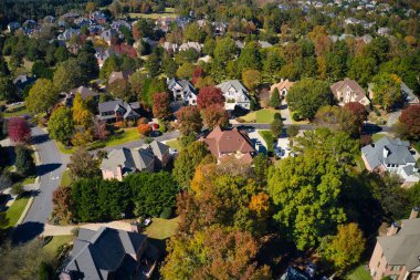 Panoramic aerial view of luxury homes in an upscale neighborhood in the suburbs with beautiful colors of leaves on the trees in the subdivision during fall of 2021. clipart