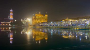 Amritsar 'daki aydınlatılmış Altın Tapınak' ın 4K videosu. Önünde su var ve kalabalık tapınağın içinde namaz kılmak için girişte bekliyor..