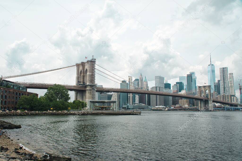 A panoramic view of Manhattan skyline and Brooklyn bridge on a cloudy day in NYC.