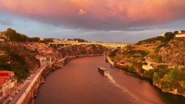 Portekiz 'in Porto kentindeki I. Luis Dom köprüsünün tepesinden gün batımında Douro nehrinde seyreden bir teknenin 4K panoramik videosu..