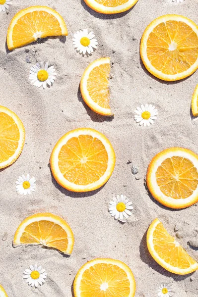 Pattern made of fresh oranges and flowers on a sandy background. Minimal summer aesthetic outdoor concept.