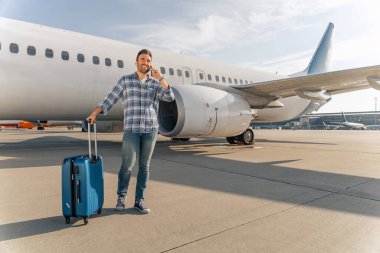 Açık havada uçağın yanında akıllı telefon kullanan gülümseyen adam.