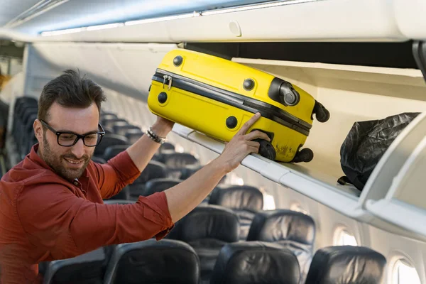 Чоловік тримає валізу і кладе її на полицю в літаку — стокове фото