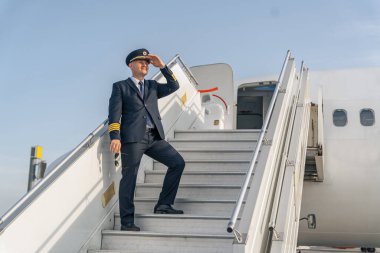 Siyah takım elbiseli pilot uçağın merdivenlerinde duruyor.