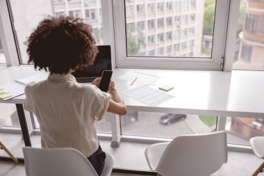 Akıllı telefonu ve laptopuyla çalışan Afro-Amerikalı kadın.