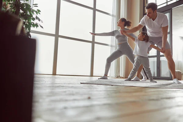 Glückliche Eltern beim Yoga mit Tochter zu Hause — Stockfoto