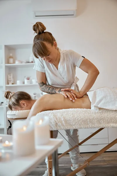 Профессиональный мастер массажа делает процедуры белой женщине в минималистичном современном кабинете — стоковое фото
