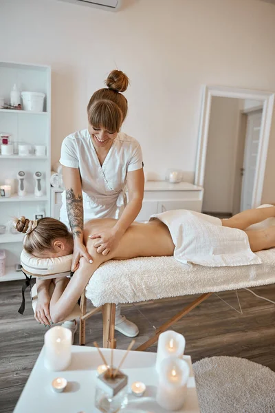 Профессиональный мастер массажа делает процедуры белой женщине в минималистичном современном кабинете — стоковое фото