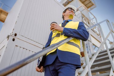 İş yerindeki erkek mühendis elinde kahve fincanı ve belgeler tutuyor.