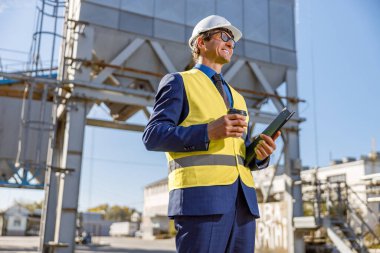 Elinde kahve ve belgeler olan gülümseyen erkek mühendis.