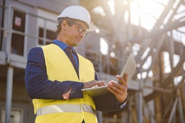 Erkek mühendis dışarıda, fabrikada defter üzerinde çalışıyor.