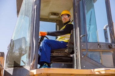 Fabrikada traktörde oturan neşeli olgun bir adam.