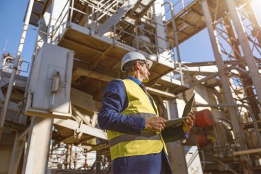 Diz üstü bilgisayarı olan erkek mühendis fabrikada bekliyor.