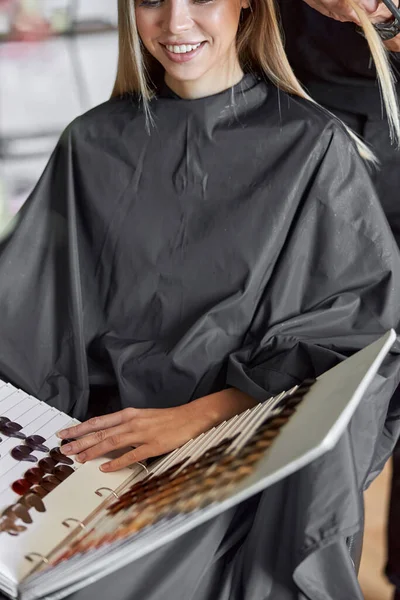 Blonde Kundin wählt Farbe in Buch, während Friseur ihr Haar schneidet — Stockfoto