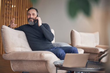 Mutlu yetişkin erkek işadamı rahat bir ofiste oturuyor ve dinleniyor.