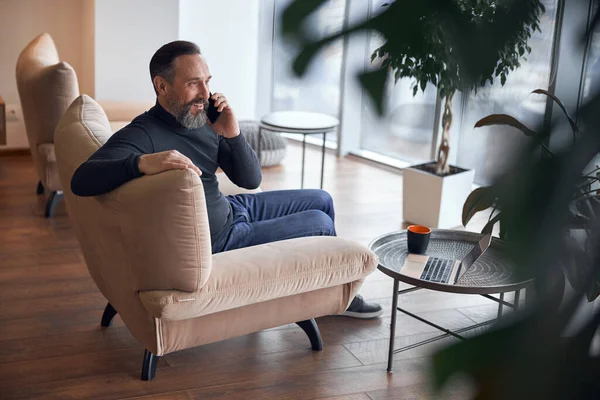 Mutlu yetişkin erkek işadamı rahat bir ofiste oturuyor ve dinleniyor.