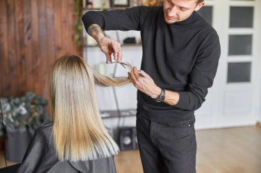 Kuaför, sarışın kadının saçlarını kesiyor.