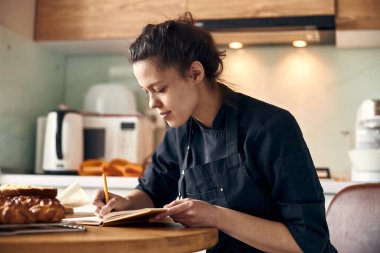Profesyonel kadın aşçı, modern hafif mutfakta eklerlerin tarifini yazıyor.