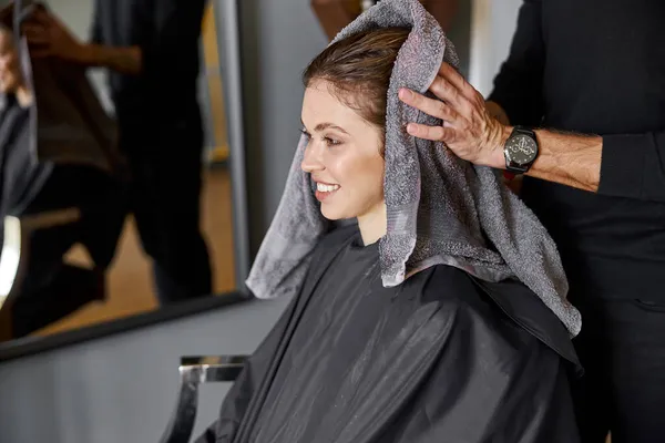 Glückliche schöne hellhaarige Kaukasierin im Schönheitssalon. Männlicher Meister trocknet ihr Haar — Stockfoto