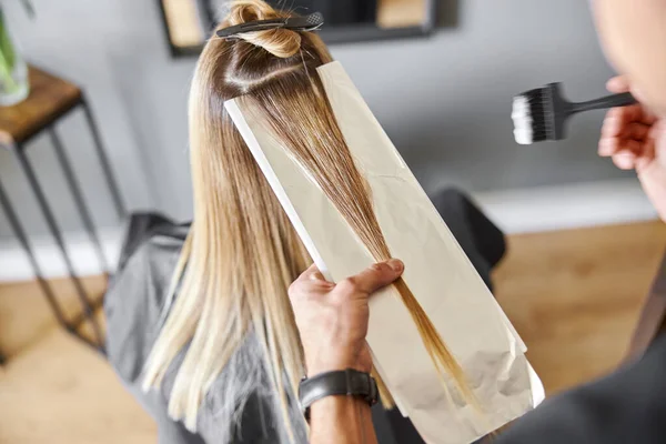 Selvsikker mannlig stylist er fargende hår på blond, kaukasisk kvinnelig klient – stockfoto