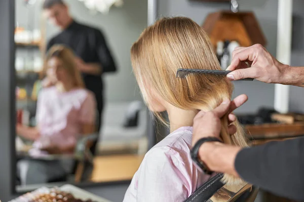 Pofessionell frisör kammar ett hår av vackra kaukasiska blond kvinna i modern salong — Stockfoto