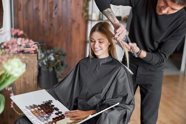 Blond kvinnlig klient väljer färg i boken medan frisören hugger håret — Stockfoto