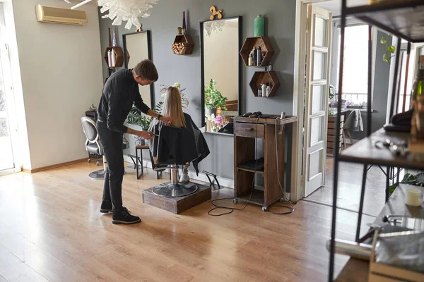 Kuaför, sarışın kadının saçlarını kesiyor.