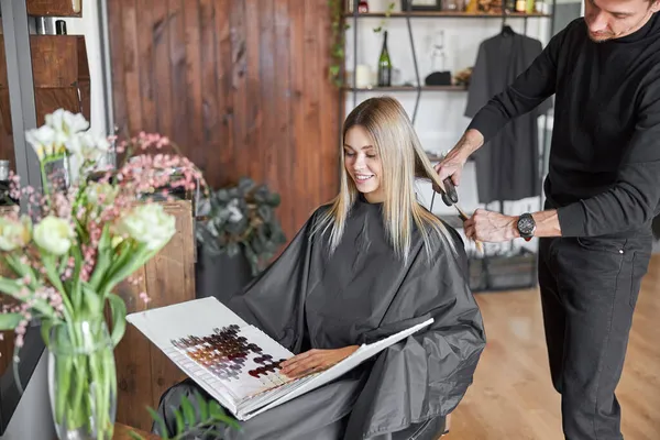Rubia cliente femenino es la elección de color en el libro, mientras que la peluquería se corta el pelo —  Fotos de Stock
