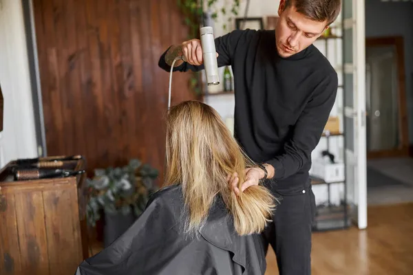 Lykkelig, vakkert hår, hvit kvinne på skjønnhetssalongen. Mannlig herre tørker håret. – stockfoto