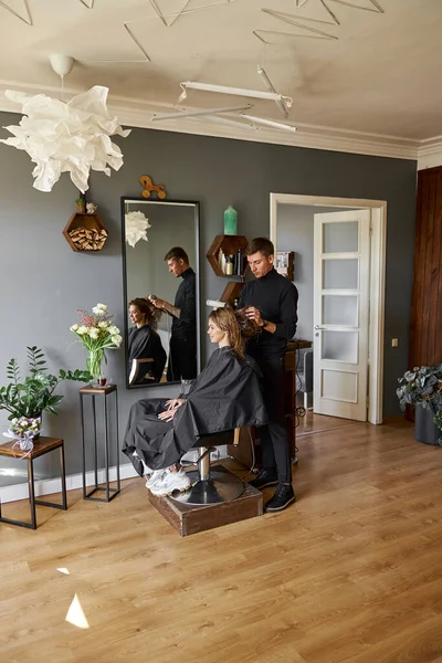 Glückliche schöne hellhaarige Kaukasierin im Schönheitssalon. Männlicher Meister trocknet ihr Haar — Stockfoto