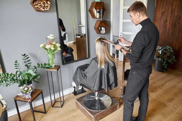 Estilista masculino seguro es teñir el cabello de rubia caucásica cliente femenino — Foto de Stock