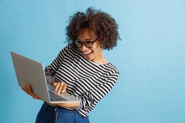 Stüdyoda dizüstü bilgisayar kullanan neşeli Afro-Amerikan kadın.