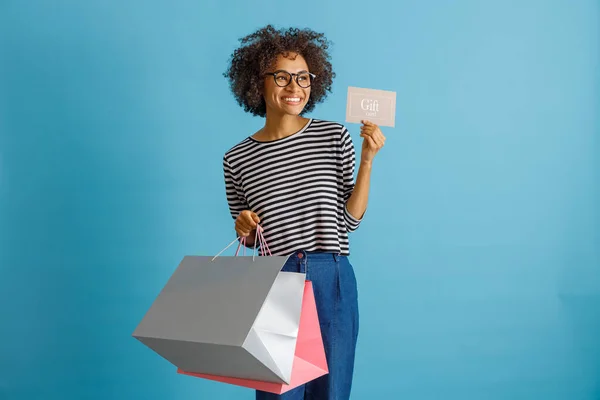 Joven alegre sosteniendo compras y tarjeta de regalo — Foto de Stock