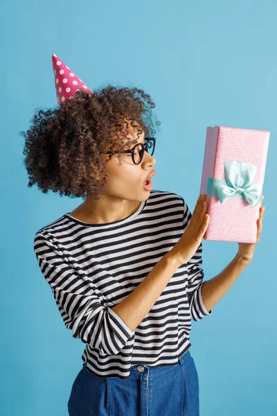 Niesamowita młoda kobieta w kapeluszu urodzinowym trzyma prezent — Zdjęcie stockowe