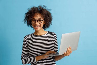 Stüdyoda dizüstü bilgisayar kullanan neşeli genç bir kadın.