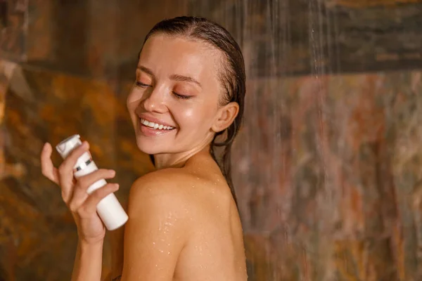 大理石のシャワーに立つ美しい若い女性の肖像画と有機自然ボディケア化粧品を使用して彼女の体を洗う — ストック写真