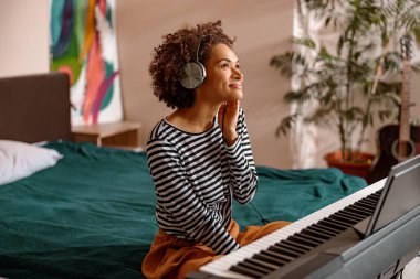 Gülümseyen kadın evde sentezleyicinin yanında oturuyor.