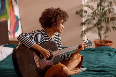Evde gitar çalan çok ırklı genç bir kadın.