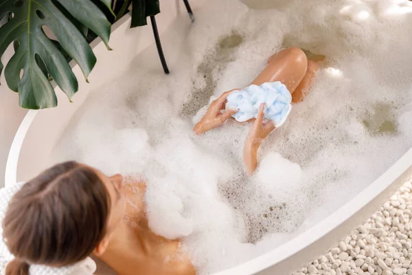 Blick aus der Vogelperspektive auf eine entspannte Frau, die sich mit Schaum in die Badewanne legt und Zeit im Luxus-Wellness-Resort verbringt — Stockfoto