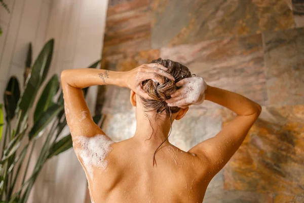 Vista posterior de la joven desnuda lavándose el pelo mientras toma la ducha en el baño — Foto de Stock