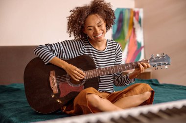 Neşeli bayan müzisyen evde gitar çalıyor.