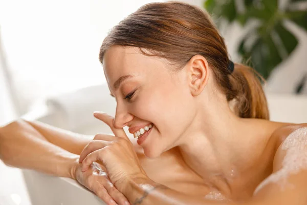 Closeup portrait of gorgeous young woman leaning on bathtub side, smiling while taking a bath — Stock Photo, Image