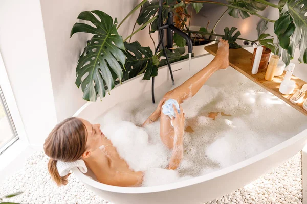 Zmysłowa młoda kobieta używająca gąbki, kąpiąca się z pianką mydlaną w luksusowym spa — Zdjęcie stockowe